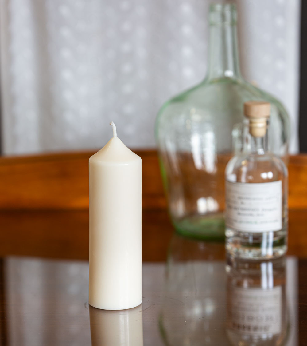 Bougie artisanale en cire naturelle de colza Ø 5 cm H 14 cm posée sur une table en verre