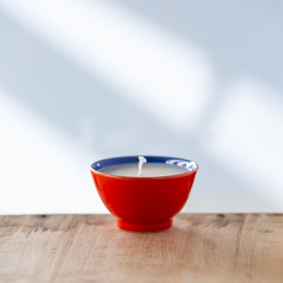 Bougie parfumée dans une tasse rouge avec bord bleu, vue de face.