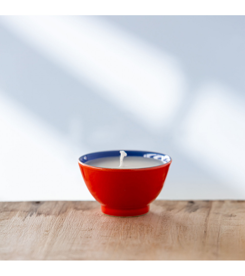 Bougie parfumée dans une tasse rouge avec bord bleu, vue de face.