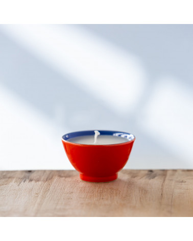 Bougie parfumée dans une tasse rouge avec bord bleu, vue de face.