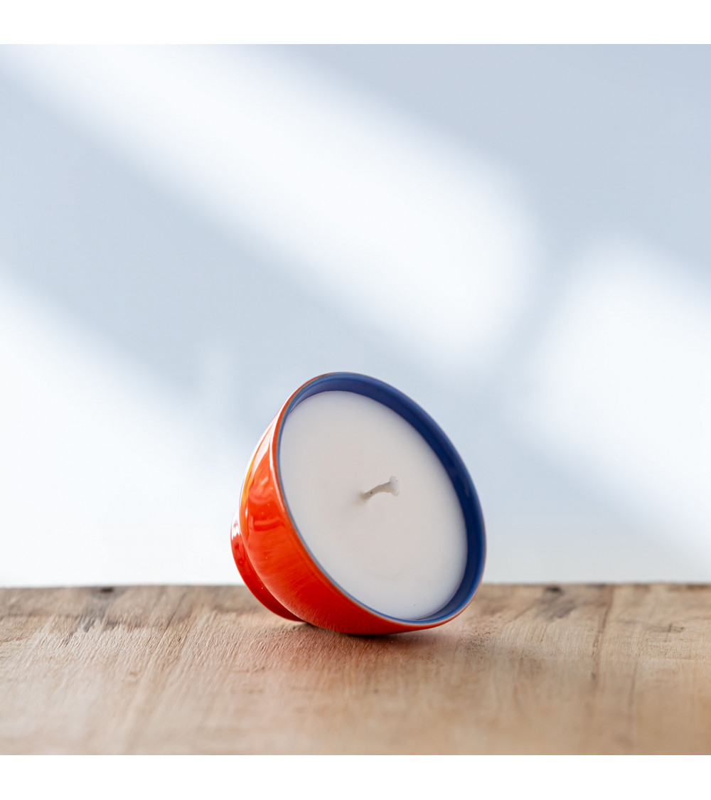Bougie dans une tasse rouge et bleu posée de biais.